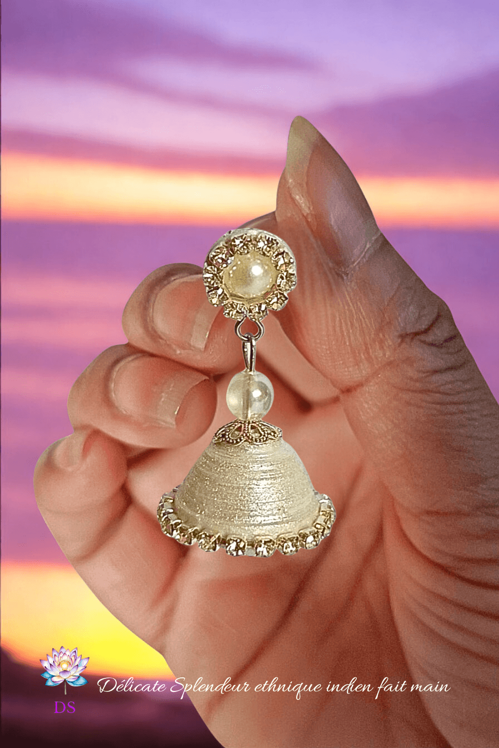 Une boucle d'oreille Djimiki Argenté simple, tenue entre les doigts, devant un coucher de soleil violet orangé.