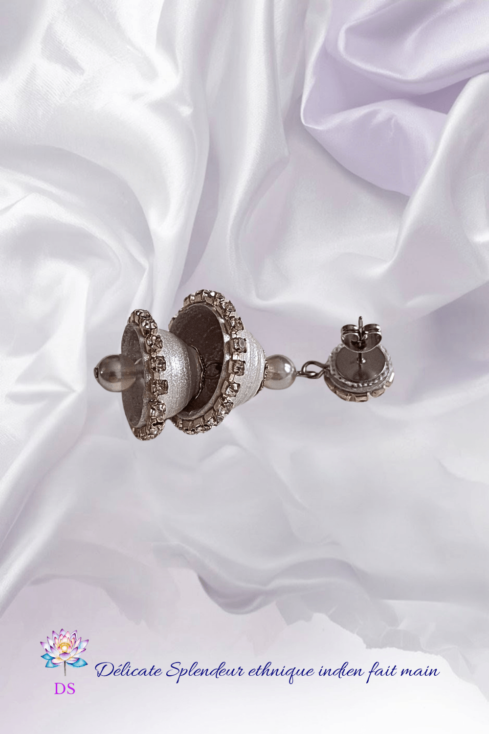 Très belle boucle d'oreille Jumka argentée, à deux étages, posée sur un tissu nacré et soyeux.