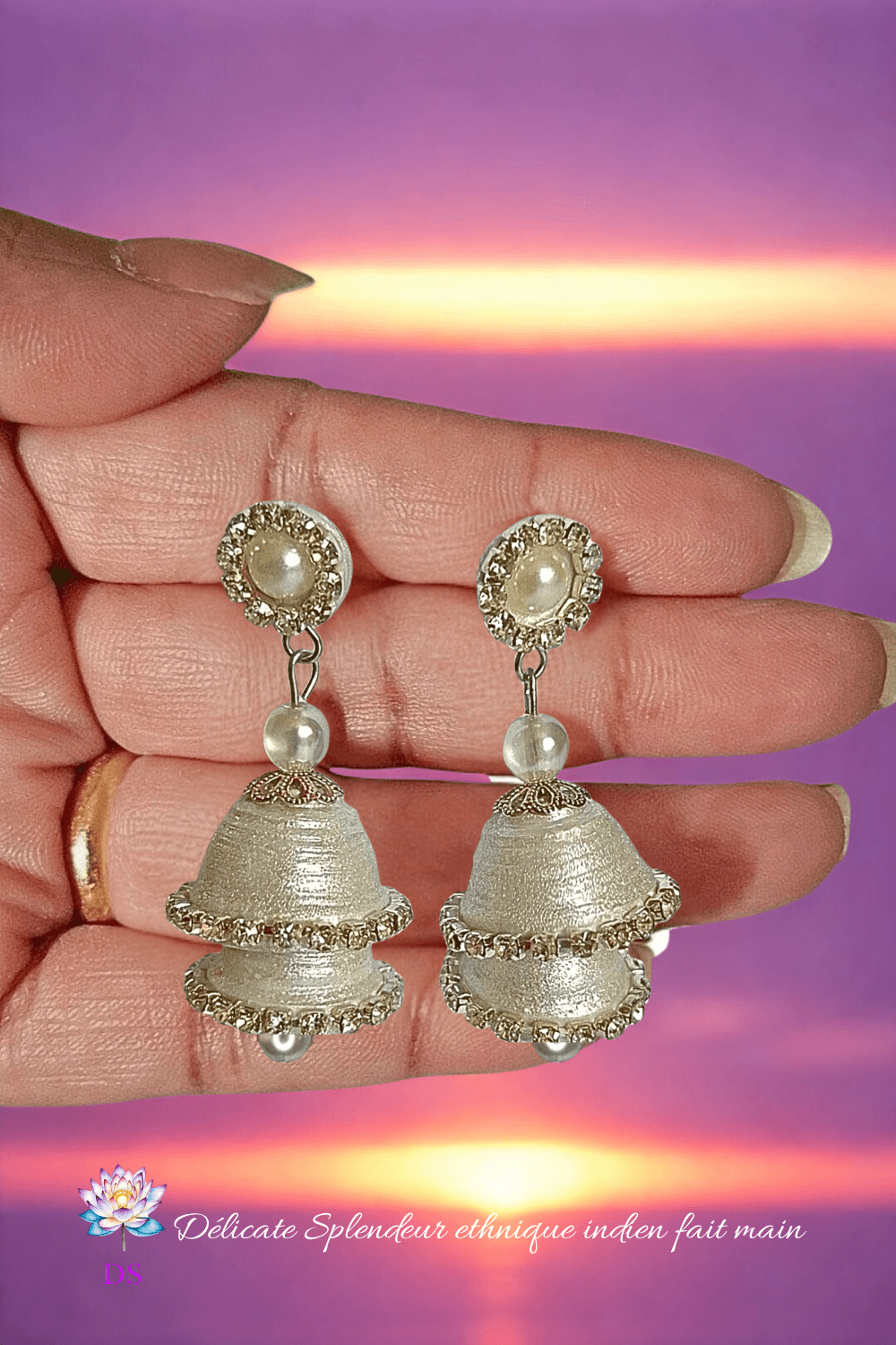Une paire de boucles d'oreilles indiennes argentées dans une main, ambiance coucher de soleil violet.