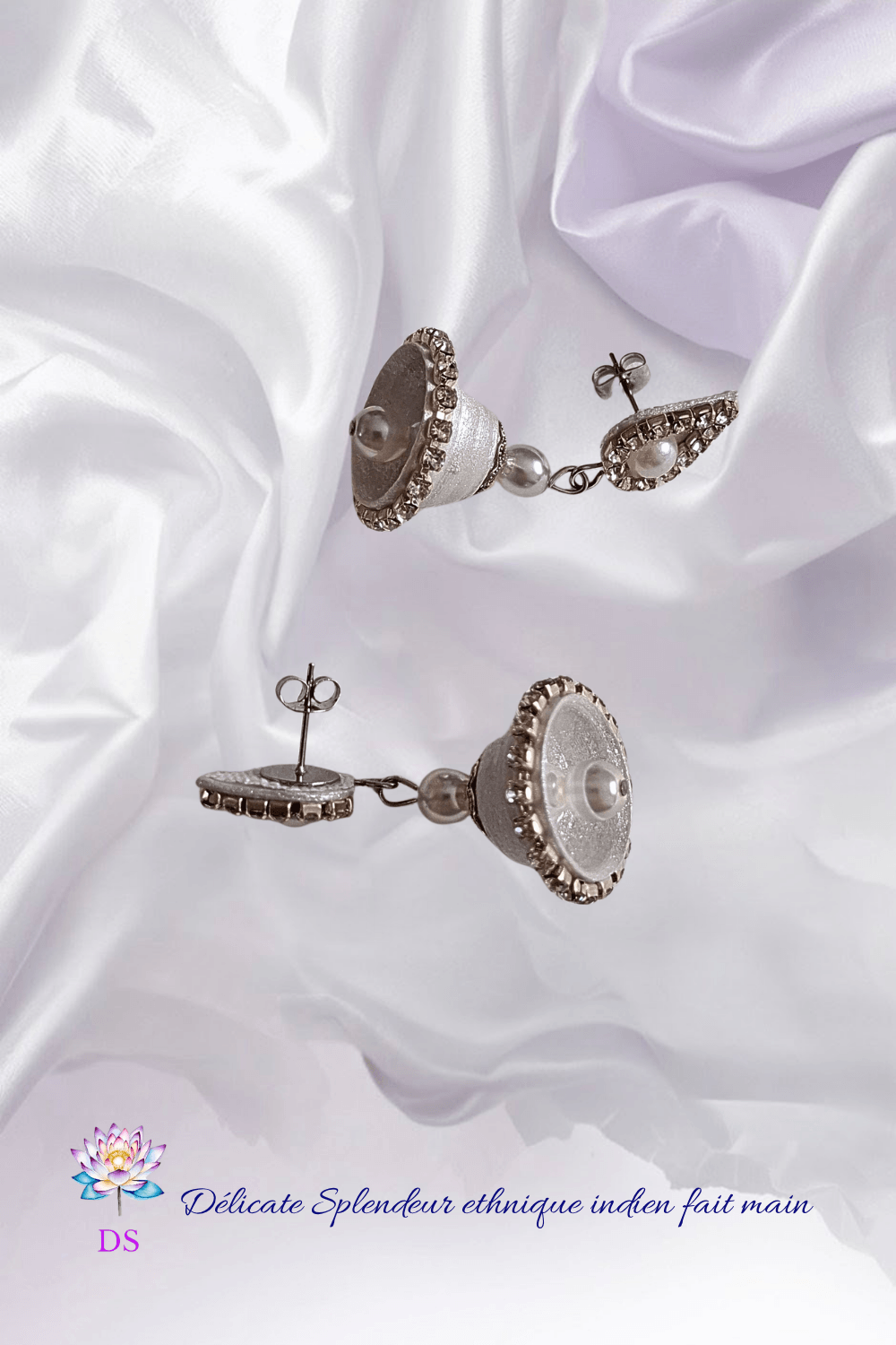 Boucles d'oreilles indiennes argentées, posées délicatement sur un tissu soyeux nacré blanc.