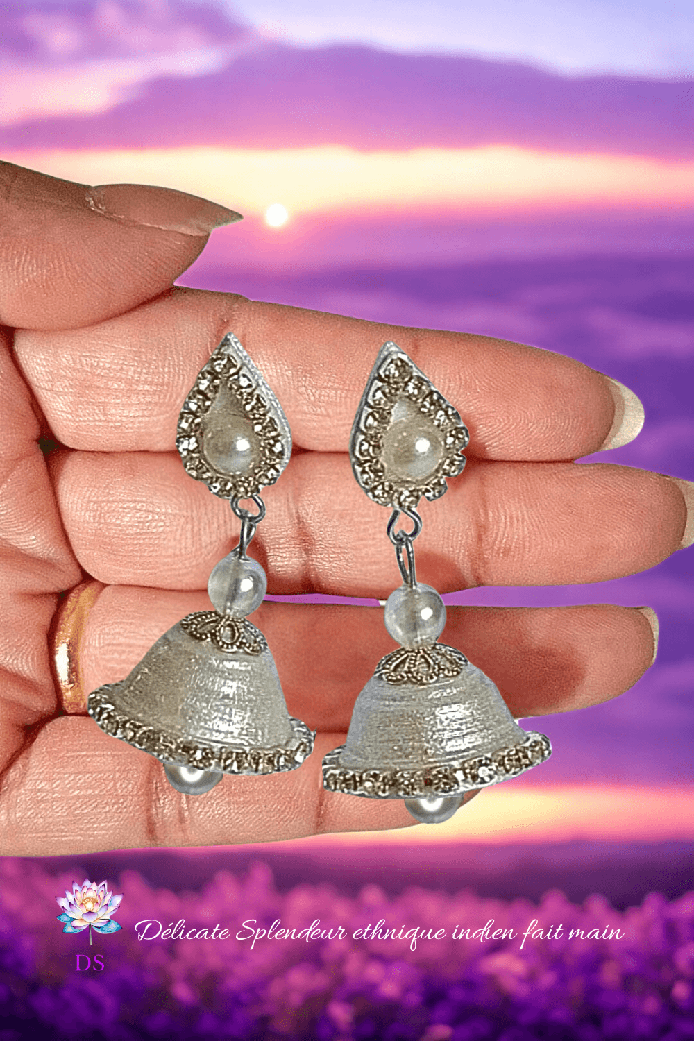 Une paire de boucles d'oreilles argentées éclatantes, dans une main, à la lumière d'une aube violette.